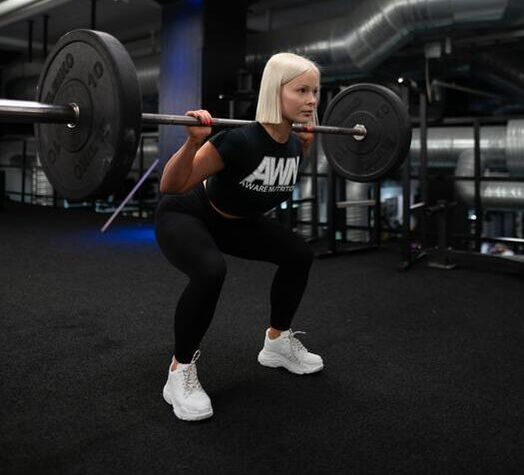 Blonde caucasian female squatting with an olympic barbell in gym with black leggings & top