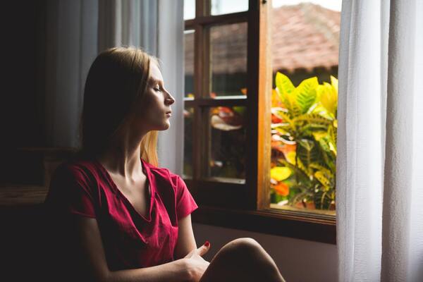 woman with eyes closed in room, window half open with plants outside